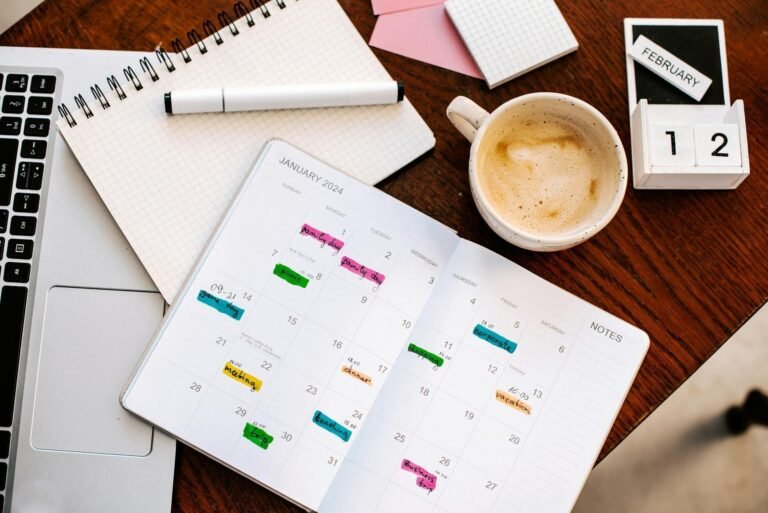 Paper planner with colour-coded entries across the month, beside a laptop and coffee