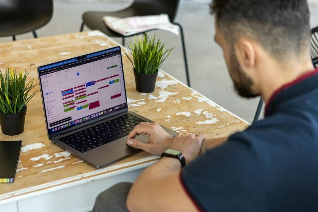 Freelancer reviewing a densely colour-blocked Google Calendar week on a laptop at a café table