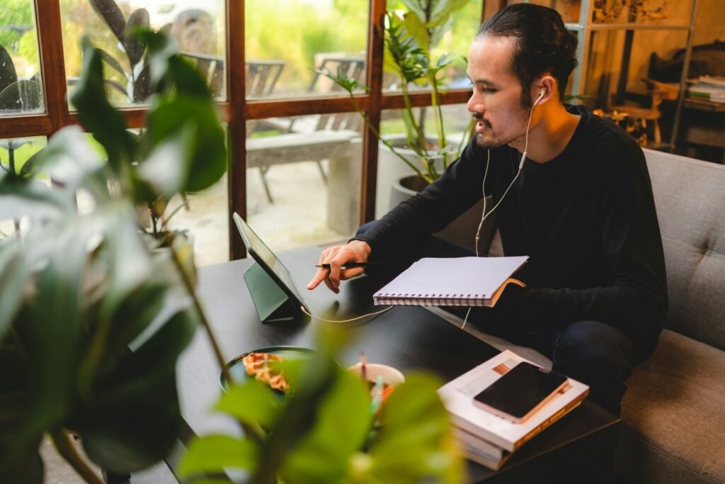 Freelancer focused on a tablet with earbuds in, working through notes in a spiral pad