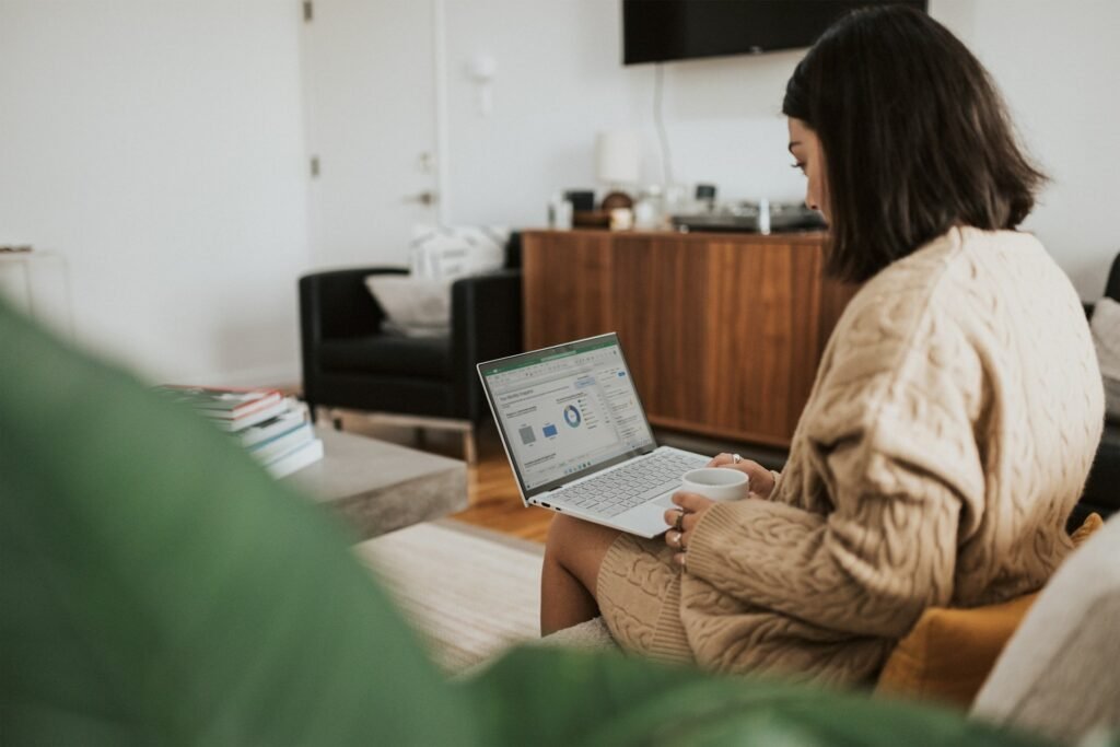 Freelancer on a sofa reviewing a monthly budget spreadsheet on a laptop