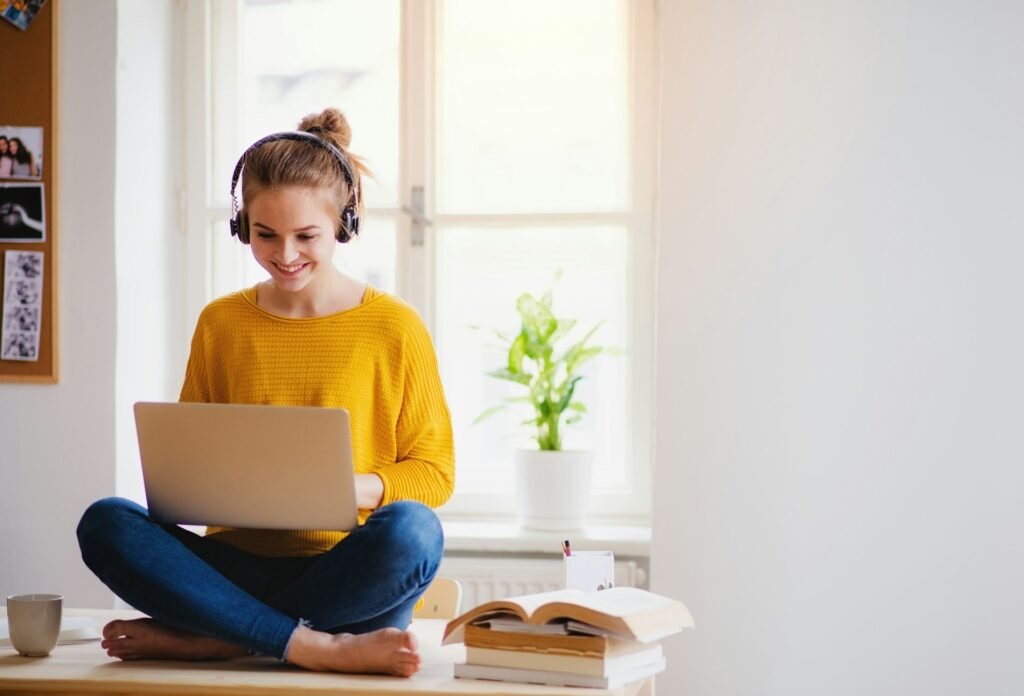 Freelancer working on a laptop while sitting cross-legged by a window