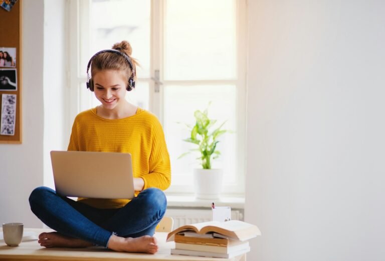 Freelancer working on a laptop while sitting cross-legged by a window