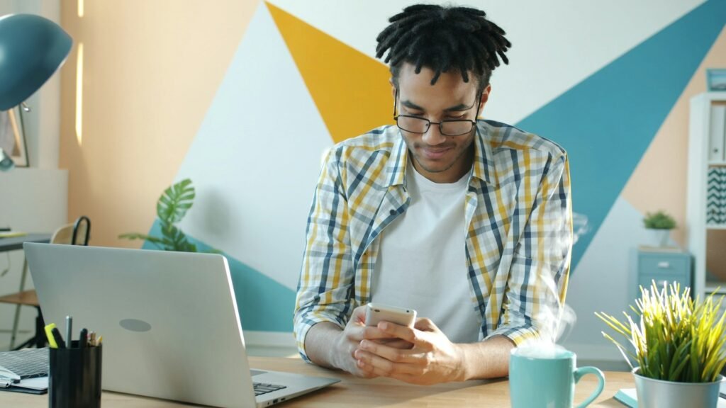 Freelancer using a phone at a desk beside a laptop in a home office