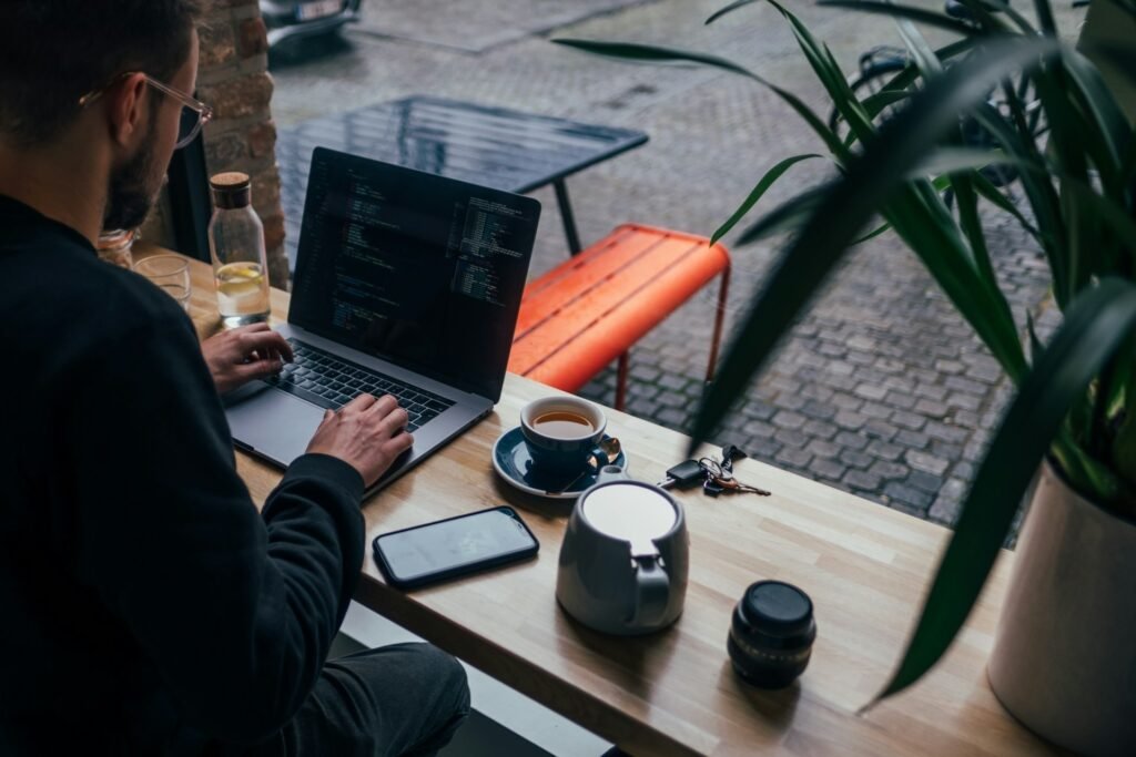 Freelancer working on a laptop at a cafe window bench, phone face-up on the table beside him