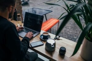Freelancer working on a laptop at a cafe window bench, phone face-up on the table beside him