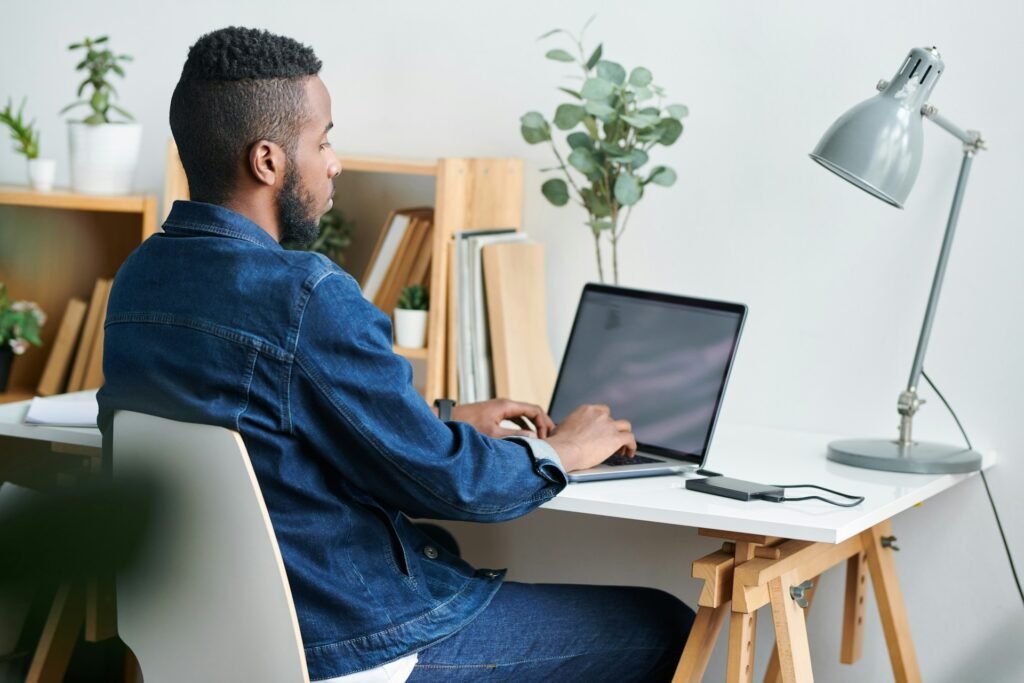 Freelancer working at a laptop in a tidy home office with plants and a lamp