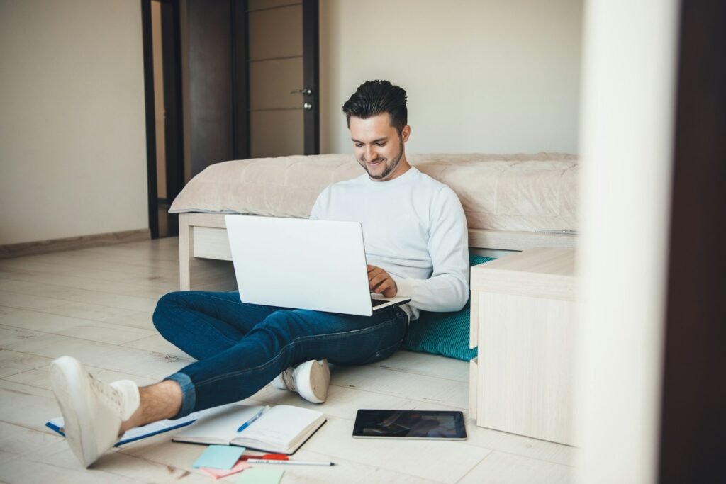 Freelancer working on a laptop on the floor with a notebook and tablet nearby