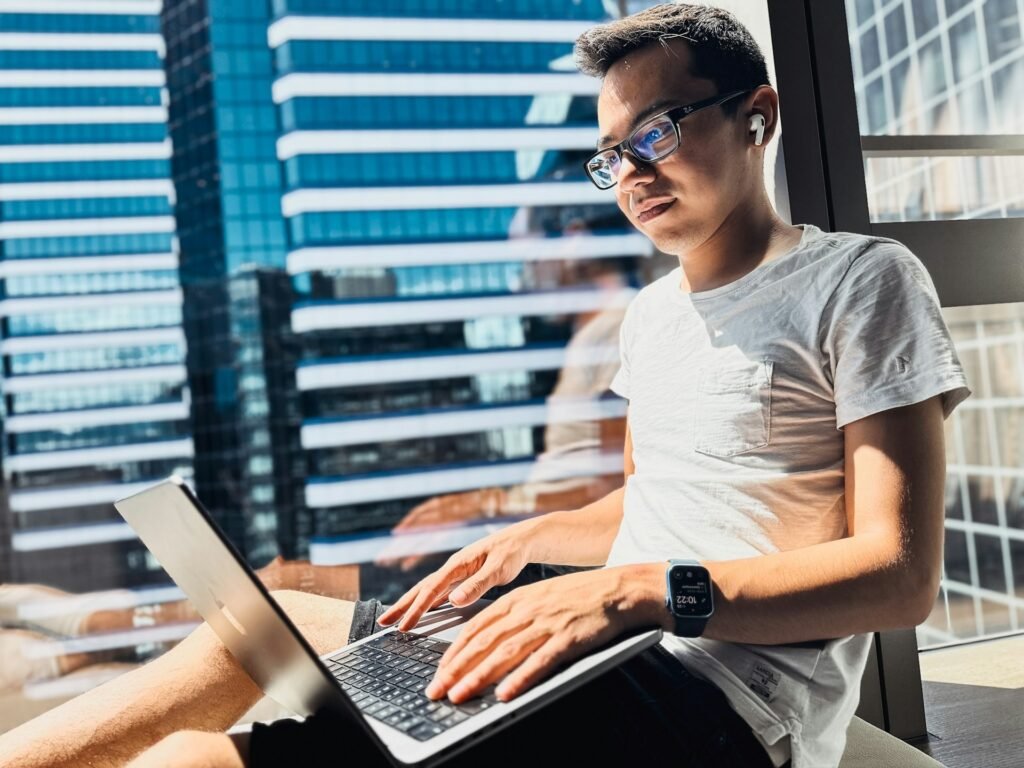 Freelancer working on a laptop by a window with an earbud in