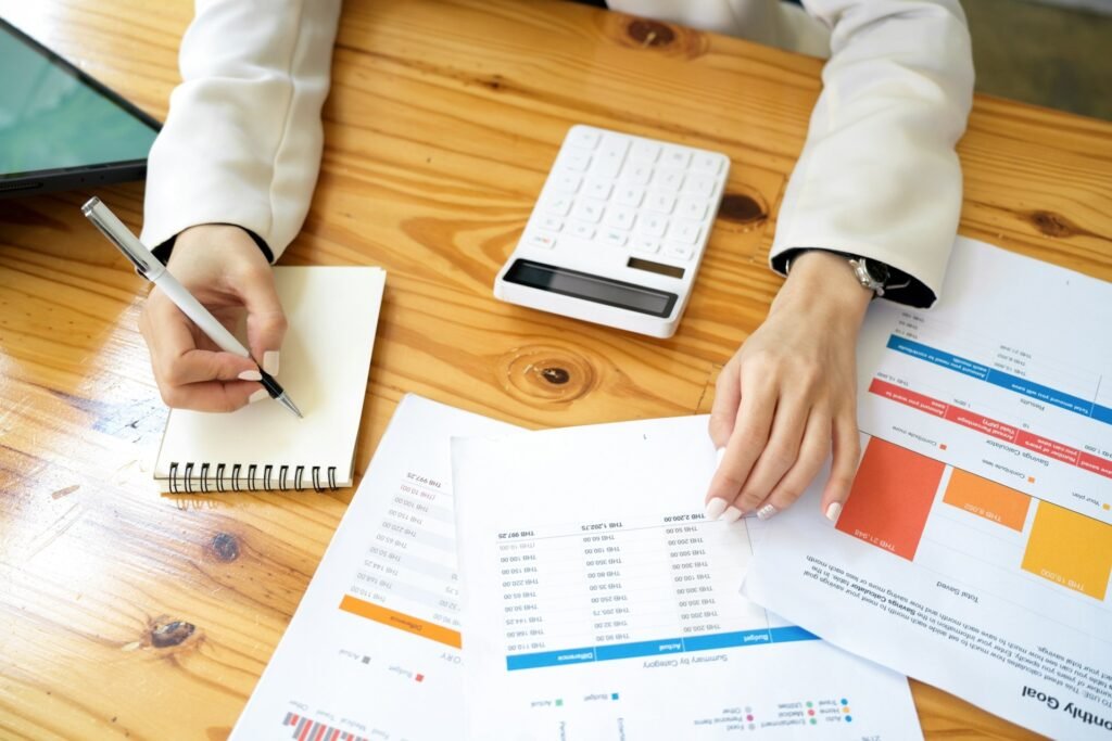 Hands writing beside a calculator and printed budget summaries with charts 