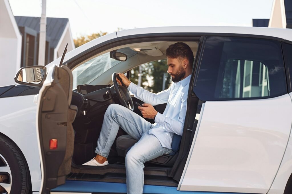 Man sitting in a parked car with the door open, checking his phone