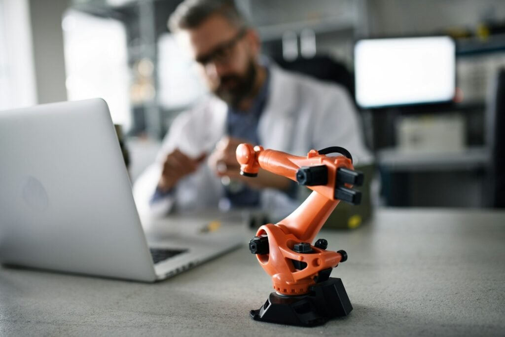 Small robotic arm on a desk beside a laptop with a technician behind, a concept image for desk-based automation in a workflow